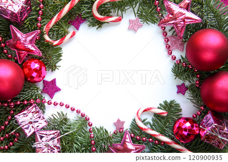 Vibrant Christmas-themed photograph features lush green fir branches adorned with fuchsia ornaments, candy canes, pink stars, shiny beads and small wrapped gifts, framing a blank white center for text 120900935