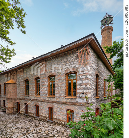 Imam Ali Mosque, a historical mosque with a tall minaret stands in a courtyard surrounded by greenery, Shaki, Azerbaijan Imam Ali Mosque, a historical mosque with a tall minaret stands in a courtyard surrounded by greenery, Shaki, Azerbaijan 120900995