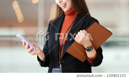 Smiling woman/businesswoman holding a smartphone and a binder 120902155