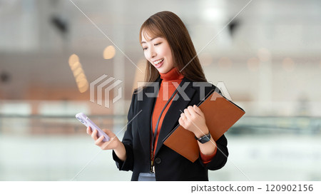 Smiling woman/businesswoman holding a smartphone and a binder 120902156