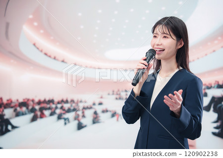 一位身穿西裝的年輕女子在大廳主持並發表演講 一位身穿西裝的年輕女子在大廳主持並發表演講 120902238