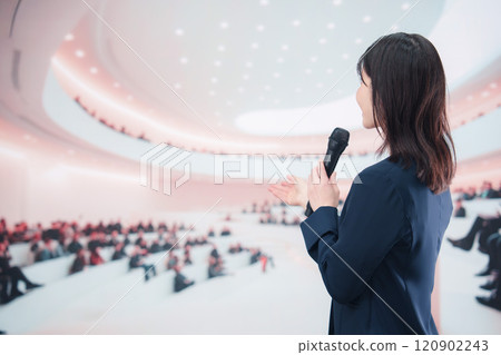 一位身穿西裝的年輕女子在大廳主持並發表演講 一位身穿西裝的年輕女子在大廳主持並發表演講 120902243