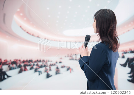 A young woman in a suit giving a presentation in a hall A young woman in a suit giving a presentation in a hall 120902245