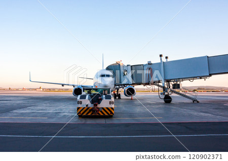 The tow tractor drive up at the passenger airplane parked to a boarding bridge The tow tractor drive up at the passenger airplane parked to a boarding bridge 120902371
