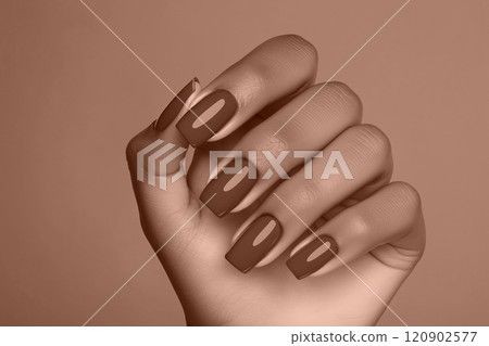 Polished mocha mousse brown nails elegantly posed against a matching backdrop 120902577
