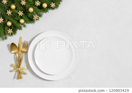 A white empty plate with fir branches and festive decorations on white background with copy space. Festive table setting for Christmas dinner. Directly above. A white empty plate with fir branches and festive decorations on white background with copy space. Festive table setting for Christmas dinner. Directly above. 120903429