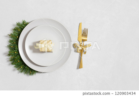 New Year table setting with gifts, fir branches and golden cutlery on white background. Christmas table. Top view, flat lay. New Year table setting with gifts, fir branches and golden cutlery on white background. Christmas table. Top view, flat lay. 120903434