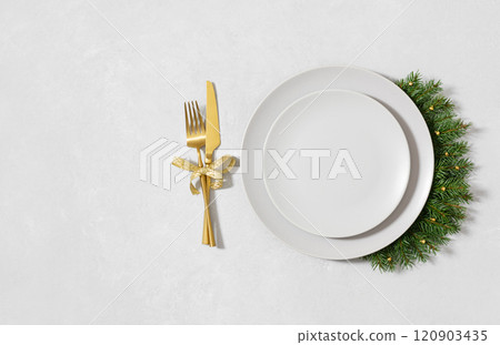 Christmas table setting with beige empty plate, fir branches and golden cutlery on white background. New Year serving for a festive dinner. Copy space. Directly above. Christmas table setting with beige empty plate, fir branches and golden cutlery on white background. New Year serving for a festive dinner. Copy space. Directly above. 120903435