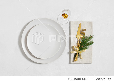 Beige empty plate with golden cutlery and a glass on white background. Christmas table setting. Happy new year. View from above. Beige empty plate with golden cutlery and a glass on white background. Christmas table setting. Happy new year. View from above. 120903436