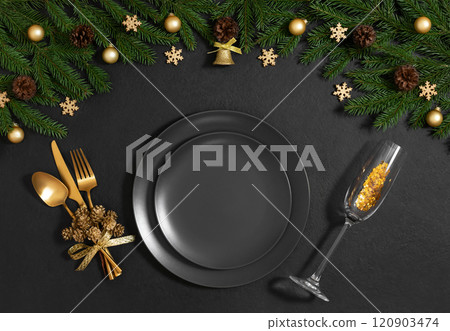 Black table setting with empty plate, gold cutlery, festive accessories and fir branches for Christmas dinner. Top view, flat lay. 120903474