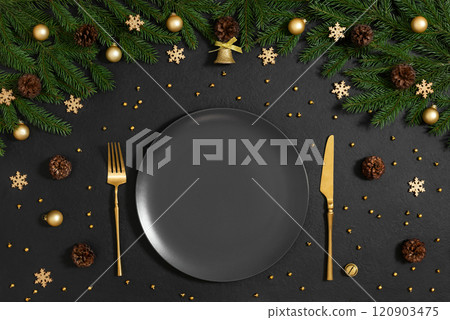 A black empty plate with gold cutlery and Christmas decorations on black background. Empty white plate for New Year serving. Top view, flat lay. A black empty plate with gold cutlery and Christmas decorations on black background. Empty white plate for New Year serving. Top view, flat lay. 120903475