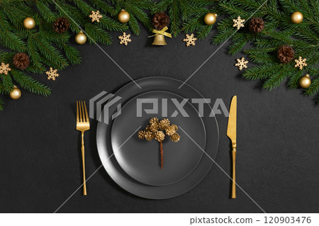 Christmas table setting with gold cutlery and festive decoration on black background. View from above. New Year serving. Christmas table setting with gold cutlery and festive decoration on black background. View from above. New Year serving. 120903476