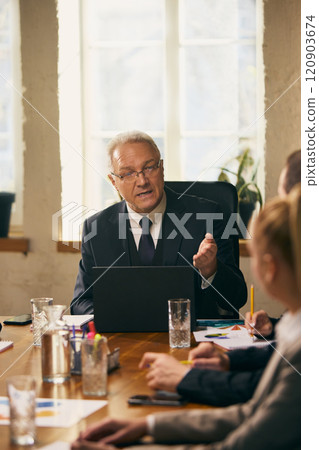 Businessman speaking confidently to colleagues at conference table, leading business conference. Working on project with team. Businessman speaking confidently to colleagues at conference table, leading business conference. Working on project with team. 120903674