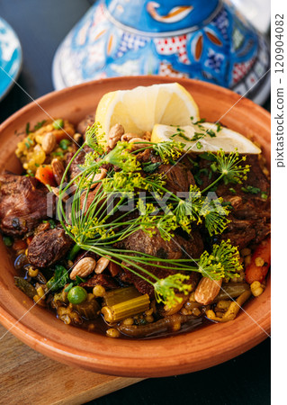 Traditional Moroccan tagine with lamb, vegetables, and nuts served with a fresh side salad. Highlights vibrant Mediterranean flavors and culinary artistry. 120904082