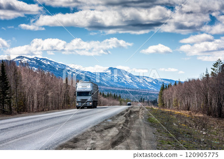 A long-distance truck with a semitrailer moves on the road among the mountains covered with snow A long-distance truck with a semitrailer moves on the road among the mountains covered with snow 120905775