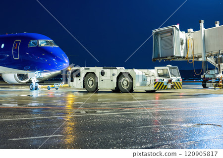 The tow tractor rolls back the passenger airplane from the air bridge at the night airport apron 120905817