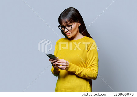 Mature smiling woman using smartphone, on grey background Mature smiling woman using smartphone, on grey background 120906076