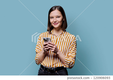 Young smiling woman using smartphone looking at camera in blue background Young smiling woman using smartphone looking at camera in blue background 120906093