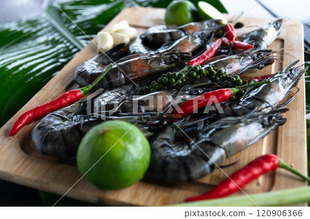 Freshly caught tiger shrimp are beautifully arranged on banana leaves, accompanied by vibrant red chili peppers, lime, and aromatic herbs, celebrating Asian culinary traditions. 120906366