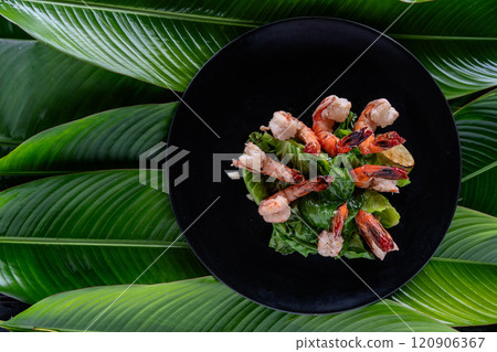 Freshly prepared tiger shrimp elegantly arranged on a bed of vibrant greens and adorned with banana leaves showcases exquisite Asian cuisine. 120906367