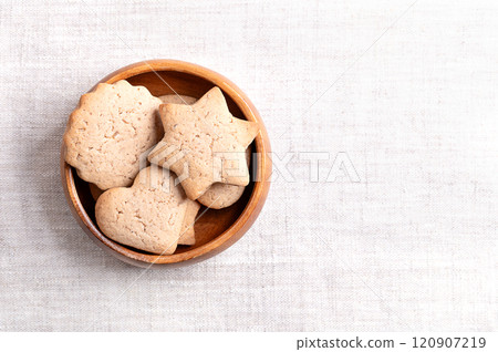 Homemade gingerbread cookies in a wooden bowl on linen fabric, with empty space for text. Sweet, light brown and flat baked goods for Christmas, flavored with ginger, cloves, nutmeg, and cinnamon. Homemade gingerbread cookies in a wooden bowl on linen fabric, with empty space for text. Sweet, light brown and flat baked goods for Christmas, flavored with ginger, cloves, nutmeg, and cinnamon. 120907219