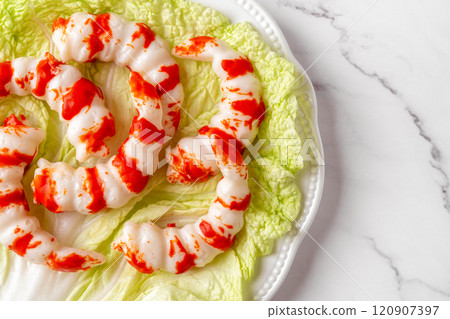 Plate with red white surimi shrimps on a green salad leaf over marble tabletop.  120907397