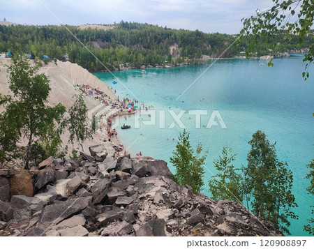 Many people swimming in the blue water near the sandy shore in a flooded quarry on a summer day. Beautiful blue water of large lake and many people swimming near the sandy shore of the slope. Top view 120908897