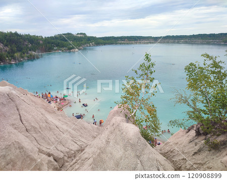 Many people swimming in the blue water near the sandy shore in a flooded quarry on a summer day. Beautiful blue water of large lake and many people swimming near the sandy shore of the slope. Top view 120908899