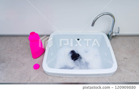 Hand-washing clothes with detergent in a sink filled with soapy water. Hand-washing clothes with detergent in a sink filled with soapy water. 120909880
