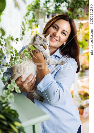 Brunette woman hugging white gray cat posing at indoor home garden together closeup 120911280