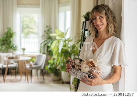 Young beautiful girl in white dress holds basket with yarn for knitting and smiles.  120911297