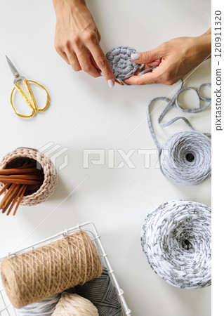 Women's hands crochet with gray yarn on a white background. Skeins of cotton yarn in natural 120911320