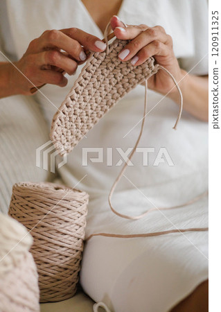 Close-up of young woman's hands. Girl crocheting from beige cotton yarn. Close-up of young woman's hands. Girl crocheting from beige cotton yarn. 120911325