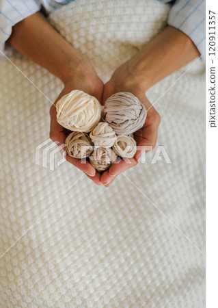 Women's hands hold balls and skeins of cotton yarn in the shape of a heart. Women's hands hold balls and skeins of cotton yarn in the shape of a heart. 120911357