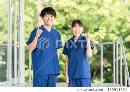 Male and female medical staff (occupational therapists, nurses, doctors, caregivers) wearing scrubs in front of a hospital or facility 120911564