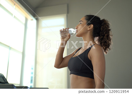Generated imageHappy sportive hispanic ethnicity woman practicing a running and cardio exercise on treadmill machine in indoor fitness club. Sportswoman drinking water in bottle during running on tre Generated imageHappy sportive hispanic ethnicity woman practicing a running and cardio exercise on treadmill machine in indoor fitness club. Sportswoman drinking water in bottle during running on tre 120911954