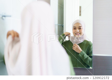 Happy Asian beautiful woman getting dressed and checking herself in front of the mirror before going to work, beautiful muslim woman looking herself in a mirror. Happy Asian beautiful woman getting dressed and checking herself in front of the mirror before going to work, beautiful muslim woman looking herself in a mirror. 120912172