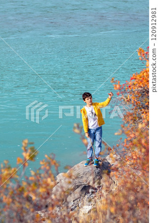 Teenage boy is enjoying a sunny fall day and the turquoise waters of the mountain river on his hike. Yellow foliage. 120912981