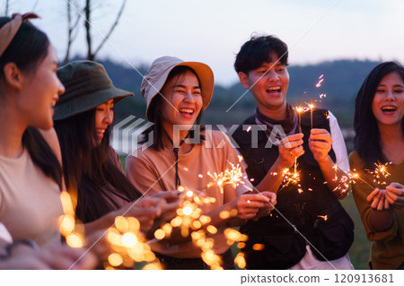 Group of Asian young men and women celebrating together with a sparkling firework in the evening. Happy men and women enjoy playing a sparklers firework in a party. 120913681
