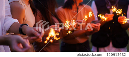 Group of Asian young men and women celebrating together with a sparkling firework in the evening. Happy men and women enjoy playing a sparklers firework in a party. 120913682