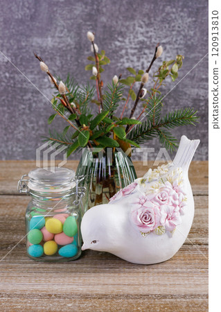 Easter colorful candies, pussywillow and a figurine of bird on the table. 120913810