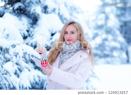 Woman in white coat with a Christmas decoration in winter forest. Woman in white coat with a Christmas decoration in winter forest. 120913857