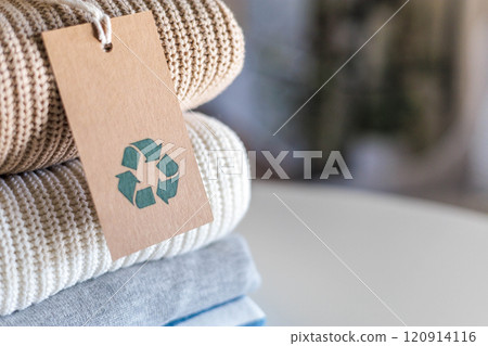 Knitted warm clothes neatly folded heap with craft tag recycling material circle arrow closeup Knitted warm clothes neatly folded heap with craft tag recycling material circle arrow closeup 120914116