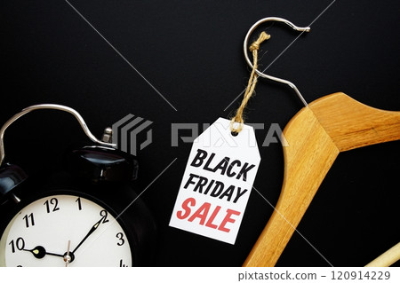 Black Friday Sale on price tag with wooden clothes hanger and alarm clock top view on black background 120914229