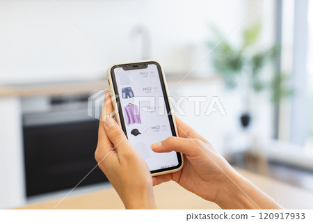 Caucasian woman browsing online store for clothing items using smartphone. Image depicts convenience of online shopping with focus on technology. Hands holding phone show webpage with clothes options. Caucasian woman browsing online store for clothing items using smartphone. Image depicts convenience of online shopping with focus on technology. Hands holding phone show webpage with clothes options. 120917933