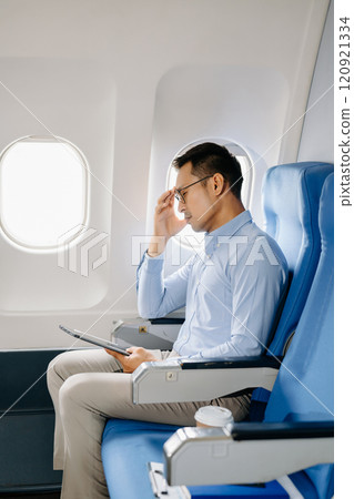 Photo of a frustrated man sitting on an airplane with her head in her hands. Asian Businessman sitting in airplane working 120921334
