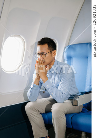 Photo of a frustrated man sitting on an airplane with her head in her hands. Asian Businessman sitting in airplane working 120921335