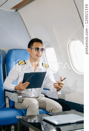 Asian Confident male pilot in uniform leaning at the passenger seat while standing inside of the airplane flight cockpit during takeoff 120921339