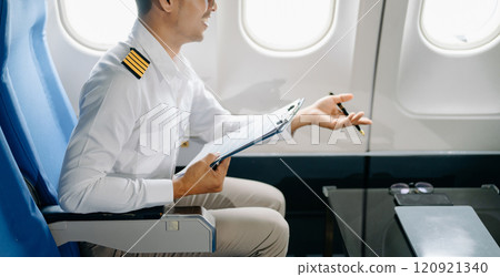 Asian Confident male pilot in uniform leaning at the passenger seat while standing inside of the airplane flight cockpit during takeoff 120921340