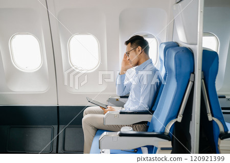 Photo of a frustrated man sitting on an airplane with her head in her hands. Asian Businessman sitting in airplane working 120921399